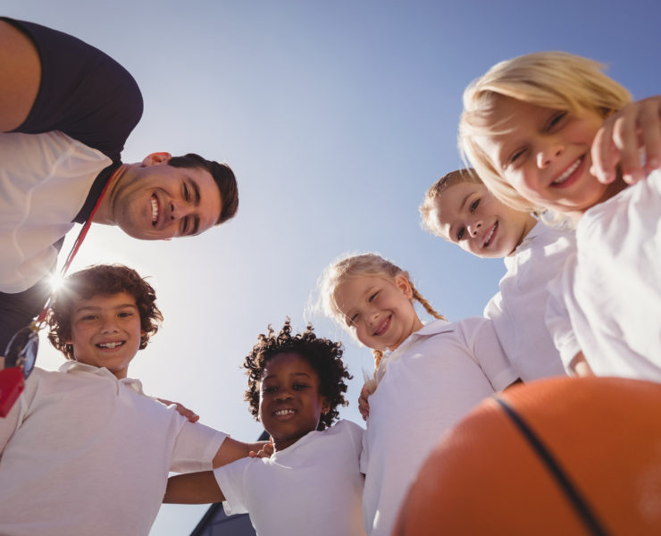 Portrait of smiling coach and schoolkids in schoolyard