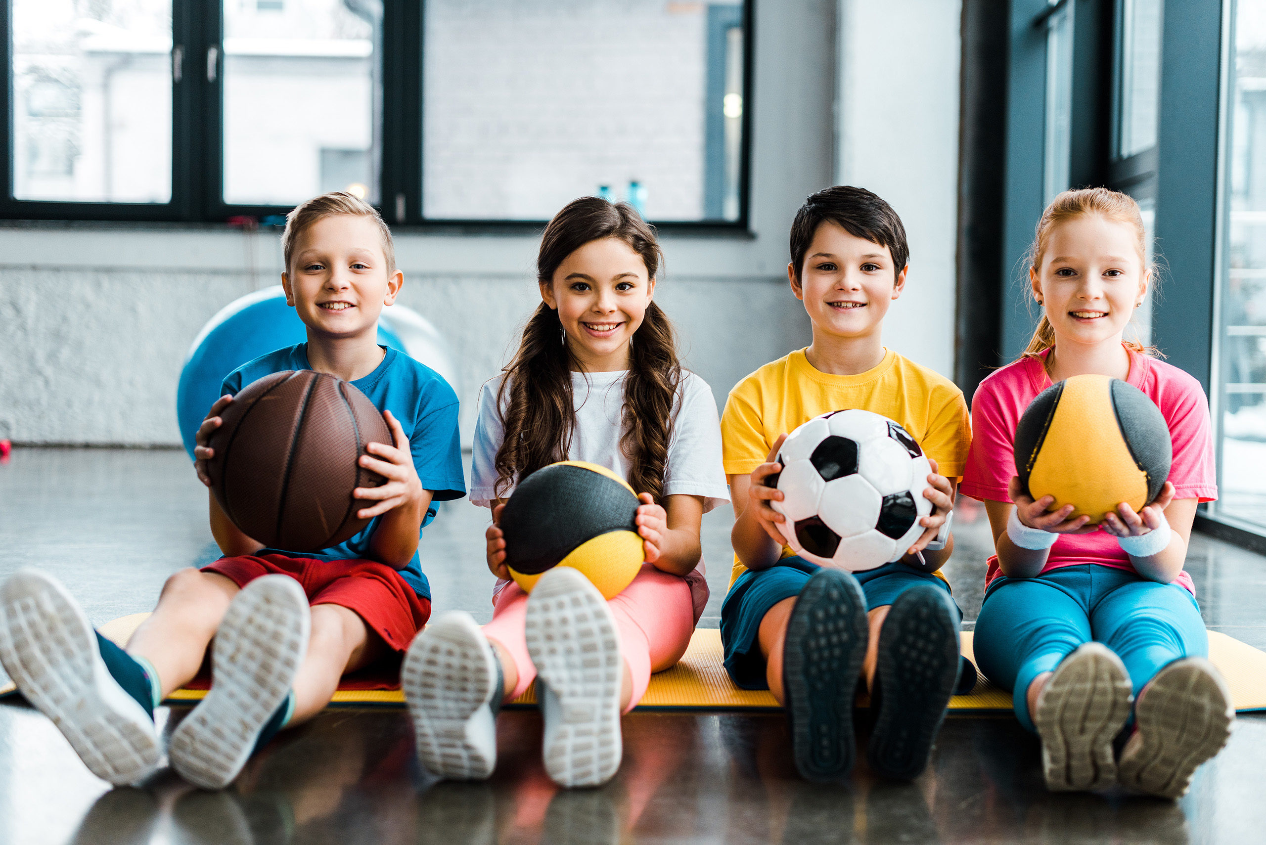 Preteen kids sitting on fitness mat with balls