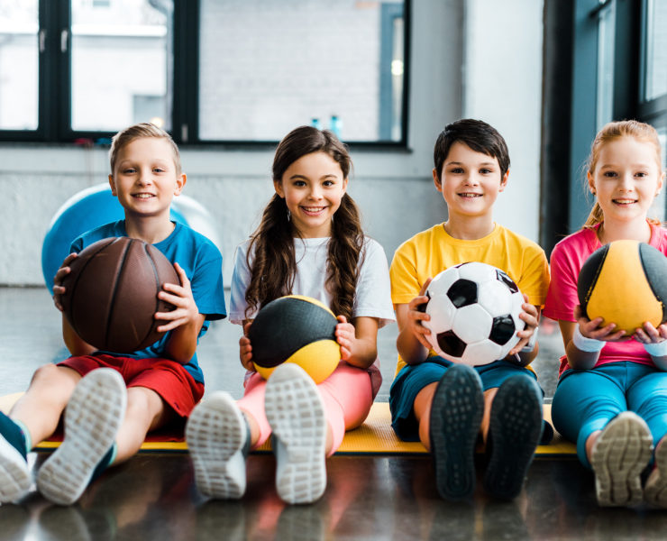 Preteen kids sitting on fitness mat with balls